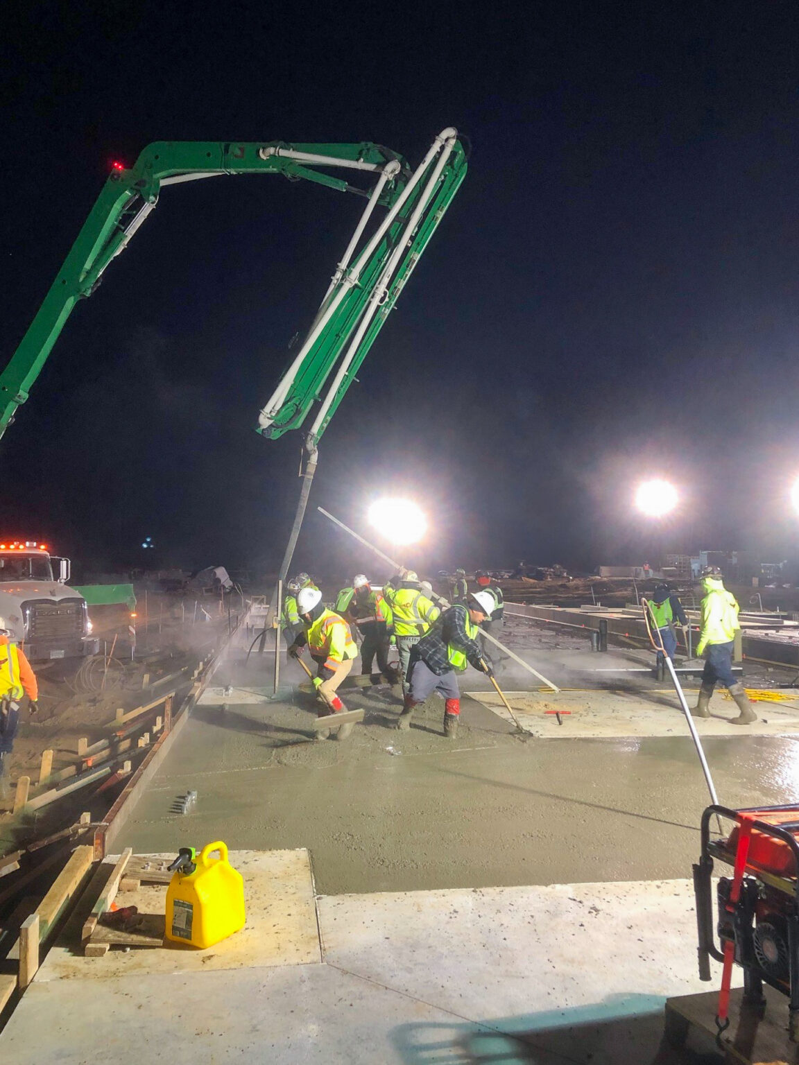 Construction crew pouring concrete at night on industrial job site